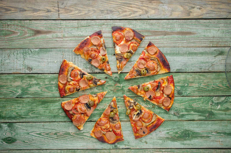 乡村绿色木桌上新鲜的切成三角形的披萨