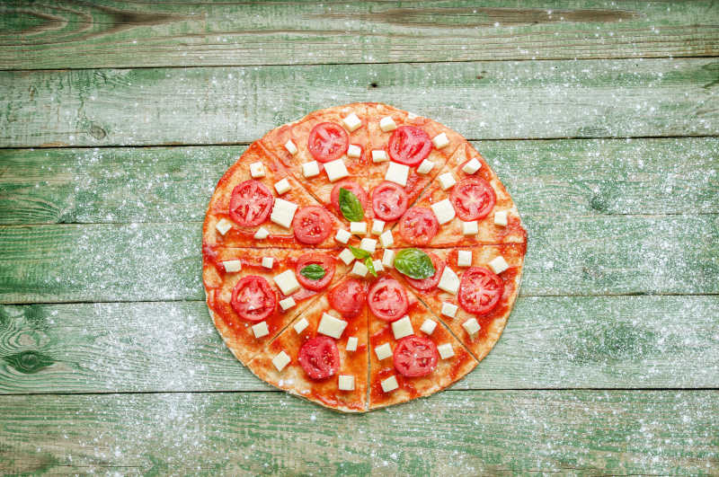 撒着面粉的绿色木桌上新鲜美味的披萨