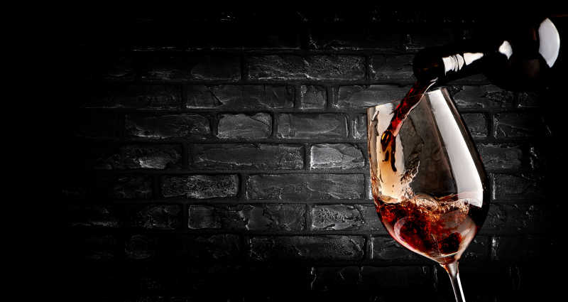 在砖墙背景上葡萄酒倒入酒杯中