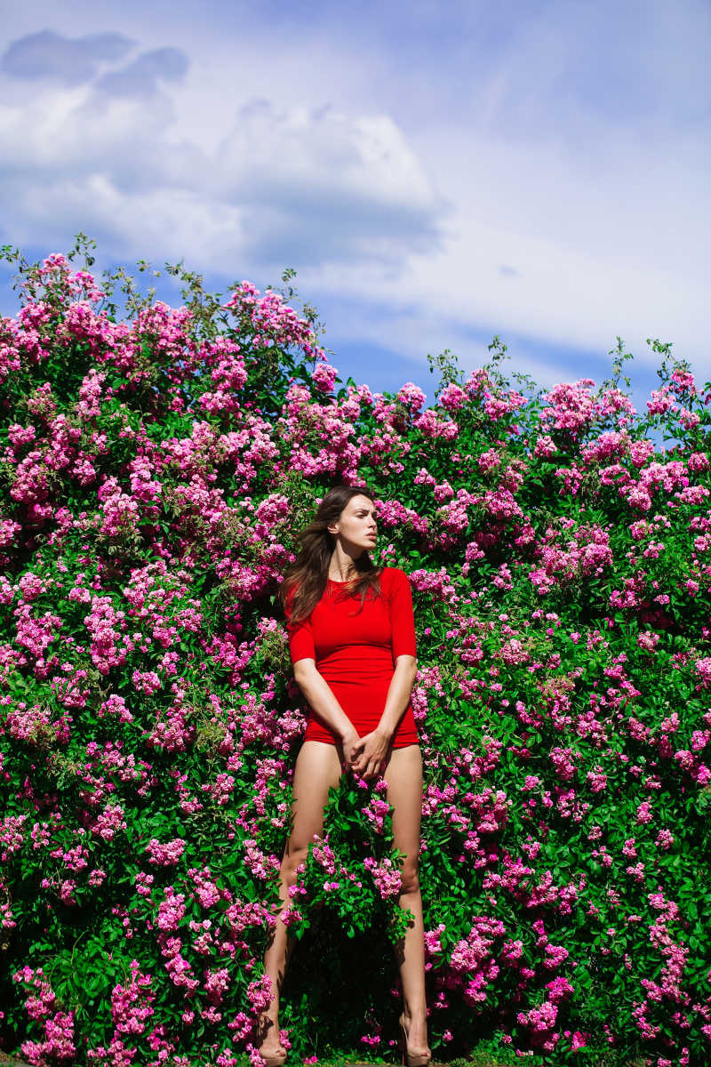 蓝天白云下站在开满粉色小花旁边的红衣美女