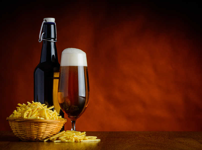 深红色背景下木桌上的啤酒和土豆条