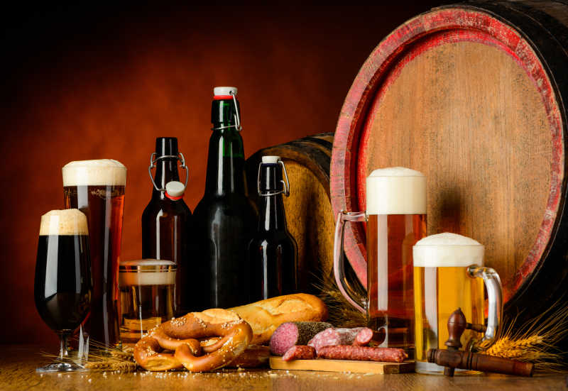褐色背景下木桌上的几瓶啤酒和一些装满啤酒的啤酒杯