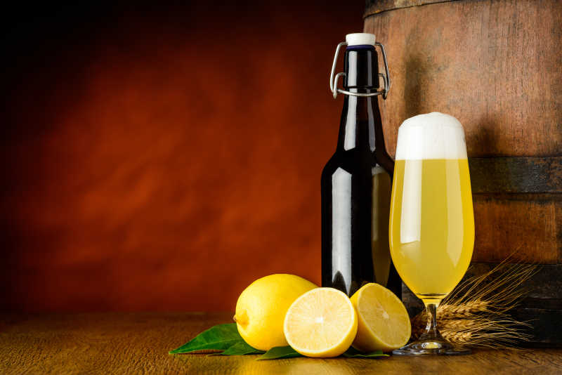 褐色背景下木桌上的柠檬拉德勒啤酒和一些新鲜柠檬