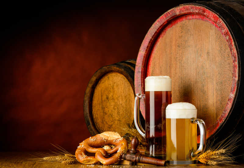 褐色背景下木桌上的两杯玻璃杯装着的啤酒和木桶