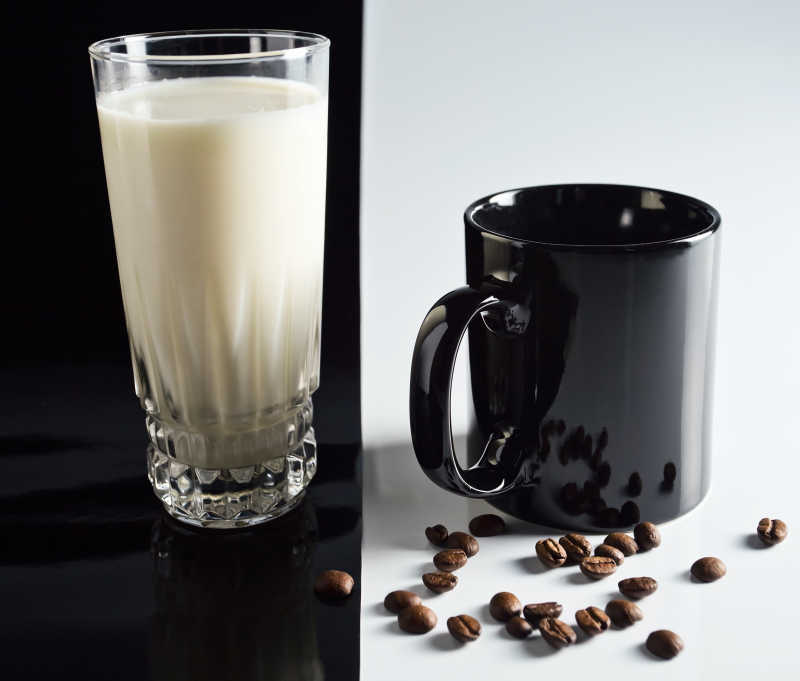 黑色背景下的一杯牛奶和黑色的咖啡杯以及咖啡豆