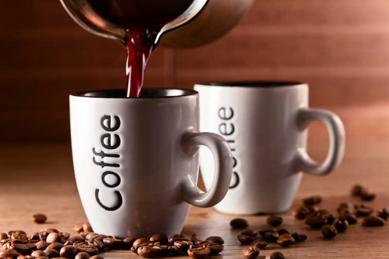 木桌上棕色的咖啡豆和白色咖啡杯倒入咖啡的瞬间摄影