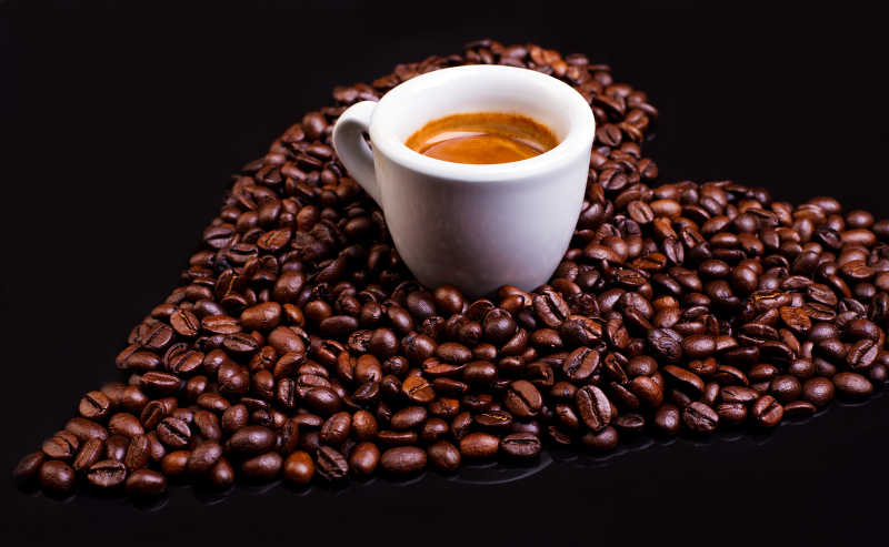 黑色桌子上的意大利浓咖啡和摆成心形的咖啡豆