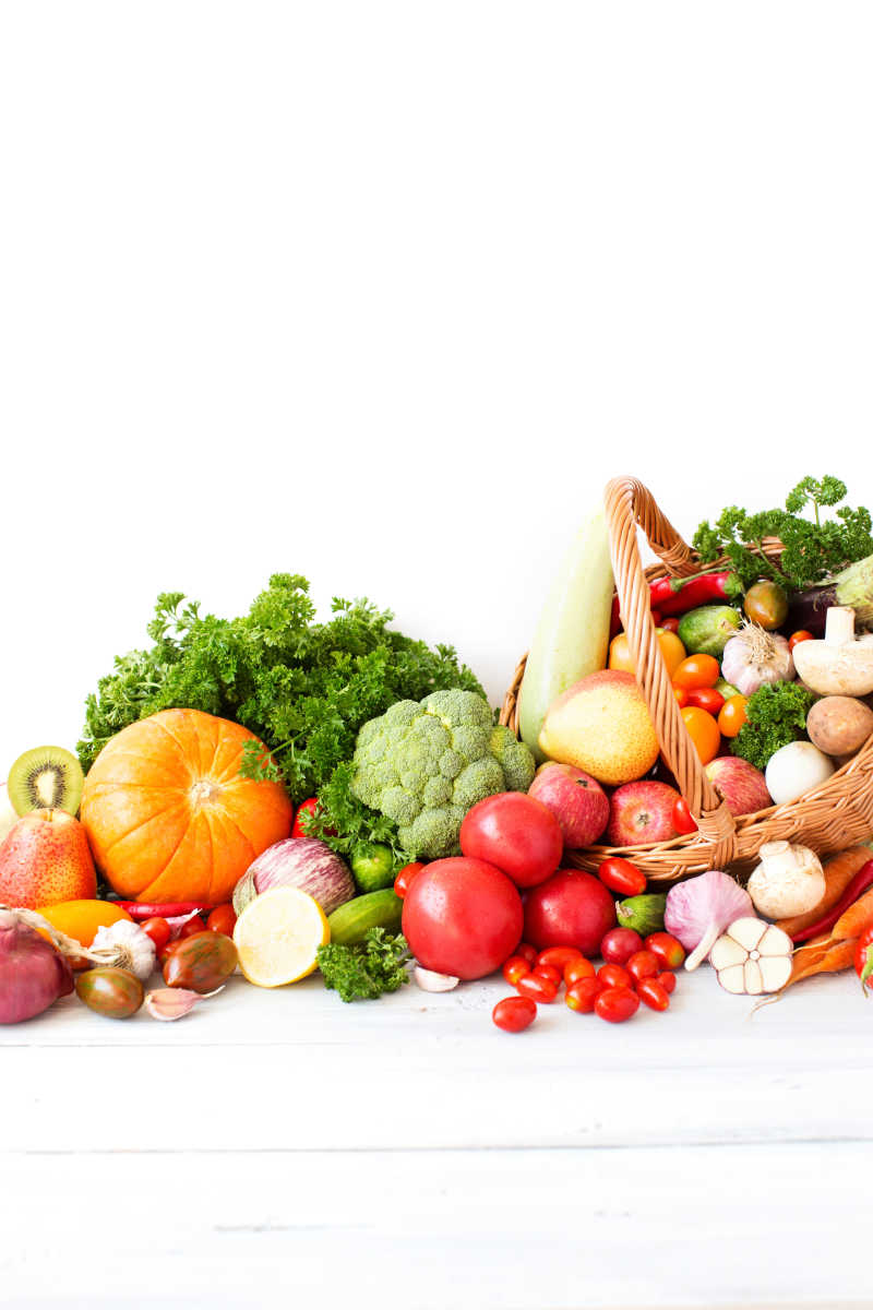 白色桌上的一堆各式各样的水果和木制蔬菜篮子里的蔬菜