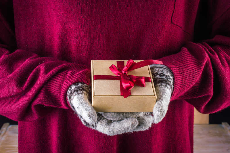 圣诞礼品盒捧在戴冬季手套女人的手上