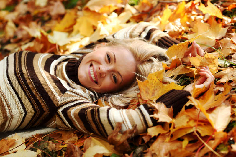 躺在秋季枯树叶上的金发美女