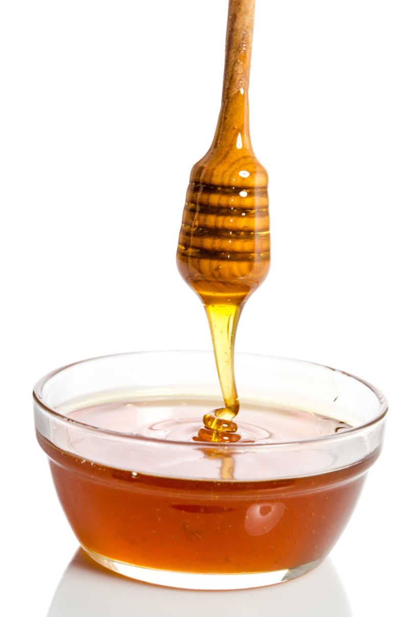 白色背景上蜂蜜从勺子里滴入玻璃碗