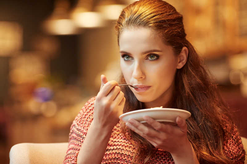 拿着盘子用叉子吃东西的美女
