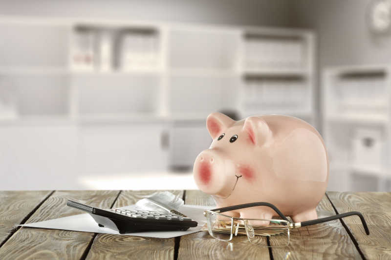 木制桌面上的小猪存钱罐和计算机眼镜