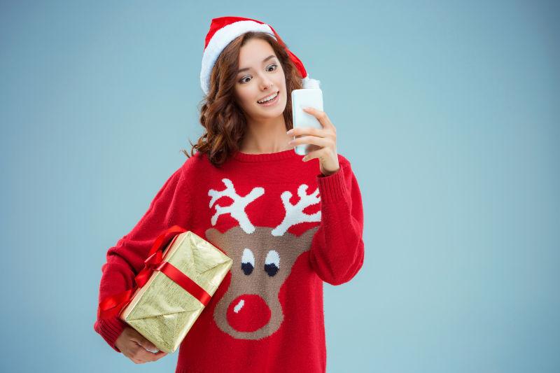 圣诞老人帽子的女孩带着圣诞礼物和电话