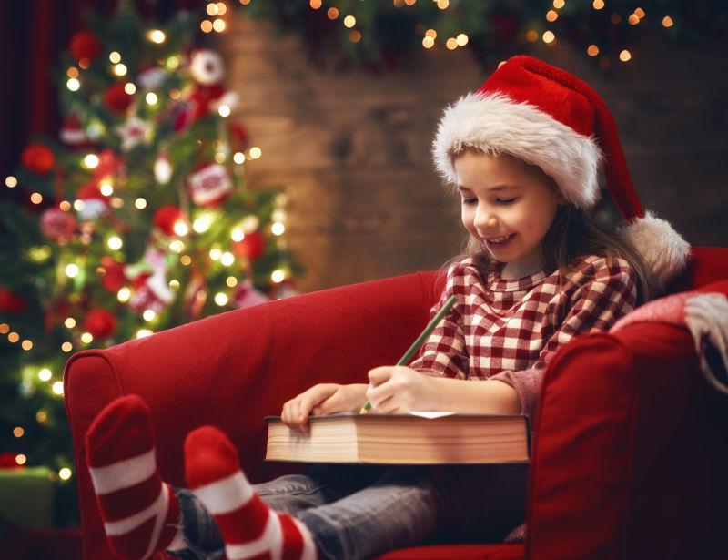 身穿圣诞节服饰坐在沙发上看书的小女孩