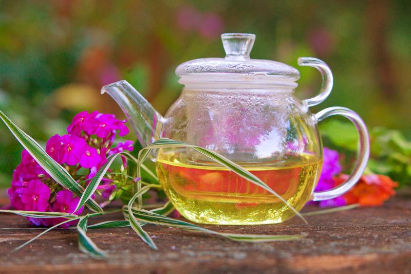 放在木桌上鲜花旁边的盛着茶水透明茶壶