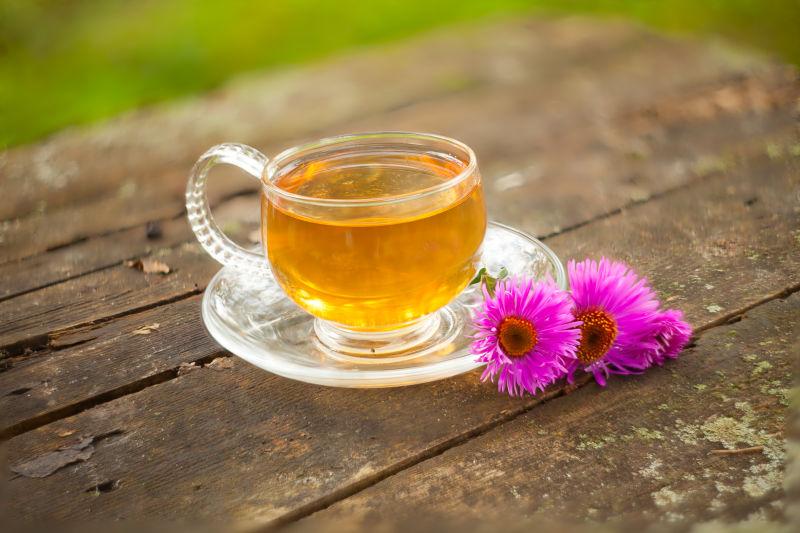木桌上紫色鲜花旁边的盛满绿茶的茶杯