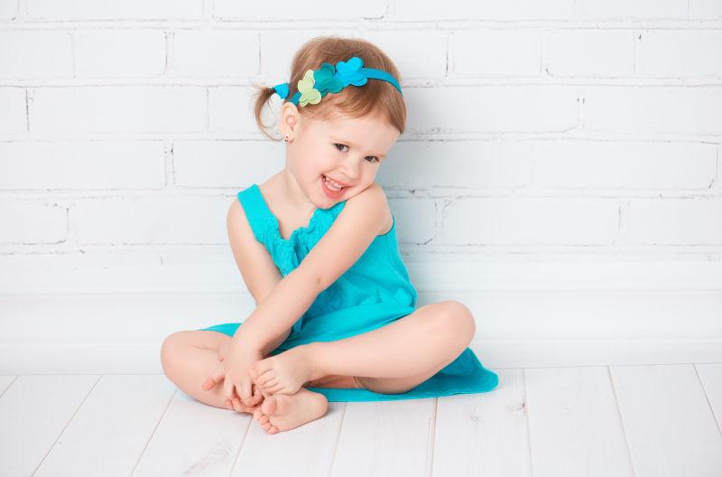 美丽的小女孩穿着一件绿松石衣服坐在地板上