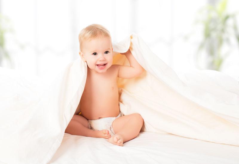 快乐的婴儿在白色毯子下笑