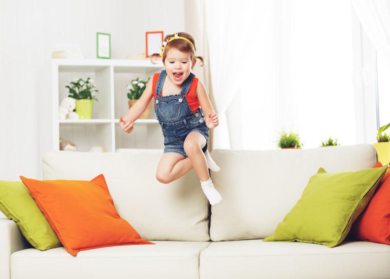 快乐的小女孩在家里的沙发上跳跃