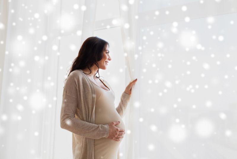 大肚子的快乐的孕妇看雪窗