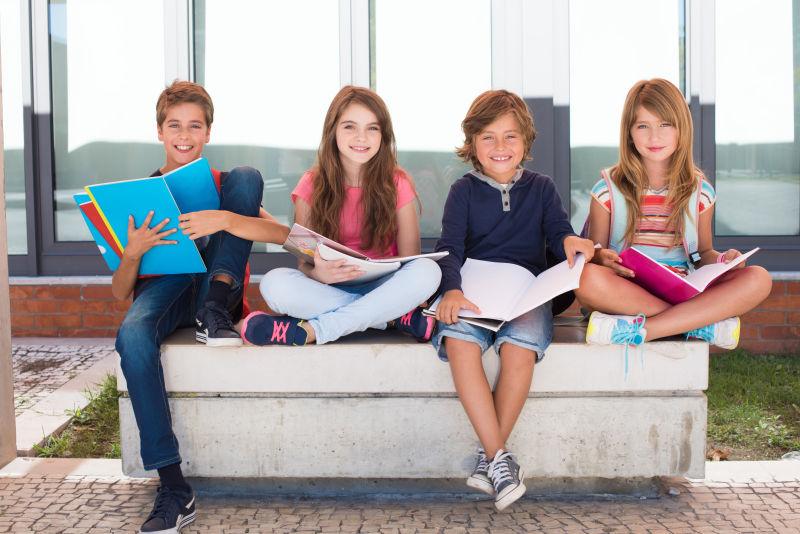 拿着书本坐在学校石凳上的四个小学生