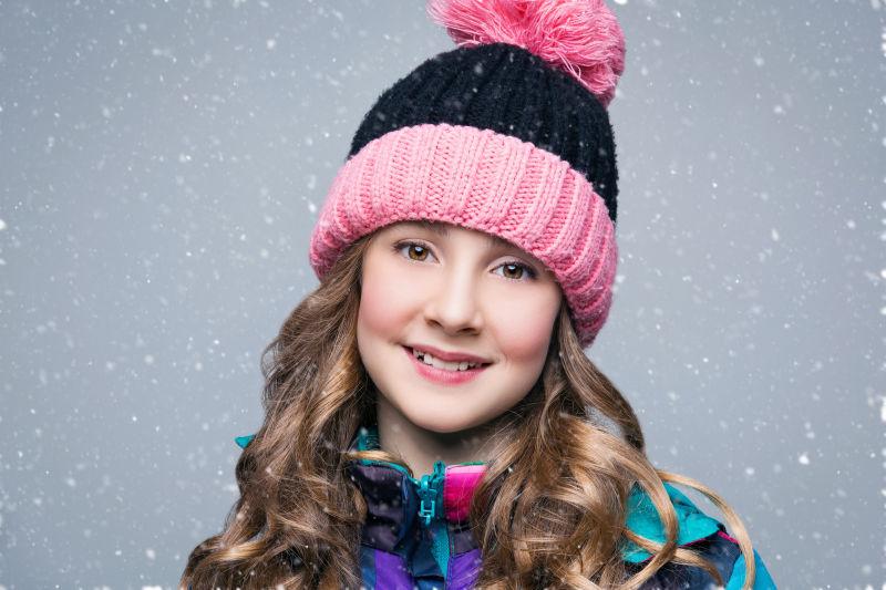 雪中戴着帽子的微笑的小女孩