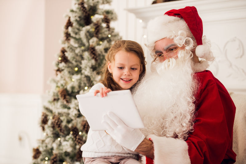 圣诞树旁边的圣诞老人在叫小女孩读书