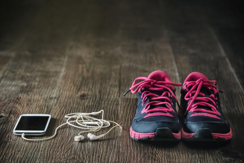 木制地板上的运动鞋手机和耳机