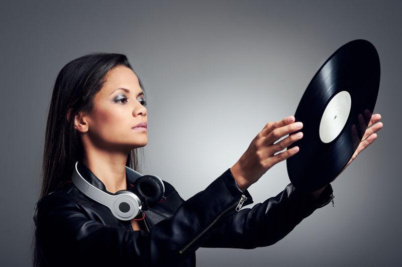 灰色背景下戴着耳机拿着黑胶唱片的女人