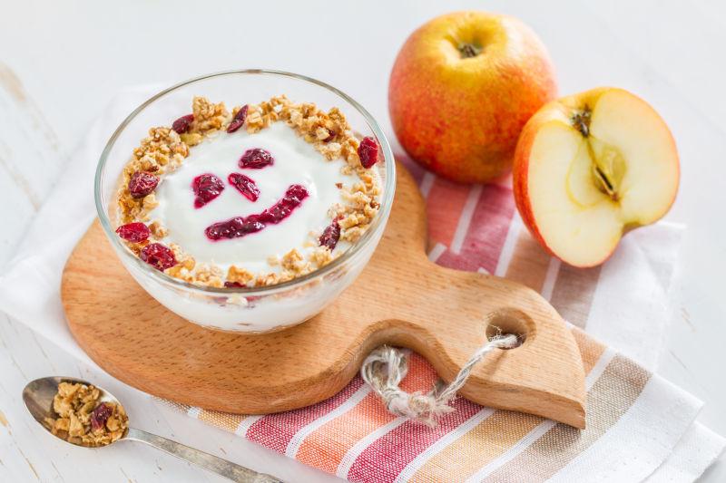 白色桌上木托盘里的坚果酸奶和苹果的健康早餐
