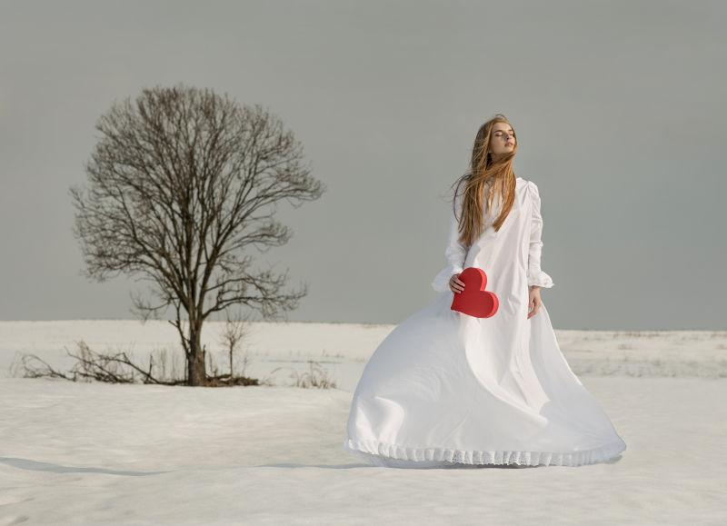 雪地里拿着红色心形的白衣美女