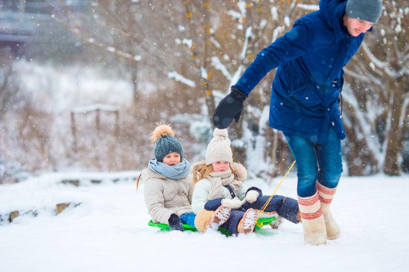 母亲与两个孩子在雪地里玩雪橇