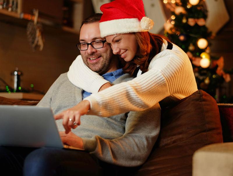 戴着圣诞帽的美女与男人看着笔记本电脑微笑