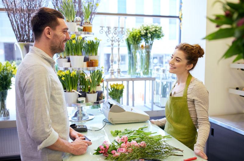 花店里的美女店员男顾客和桌上的修剪花枝