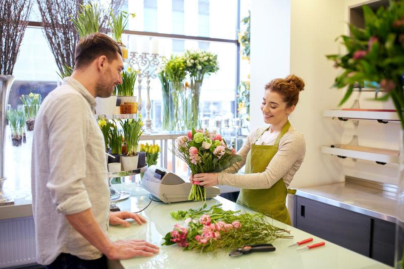 花店里的美女店员为男顾客修剪挑好的花束枝叶