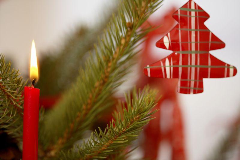 枝头上挂着的红色圣诞树装饰品和旁边点燃的红色蜡烛