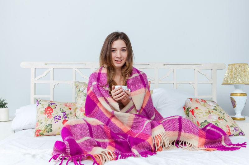 生病的女人裹着毯子拿着茶杯