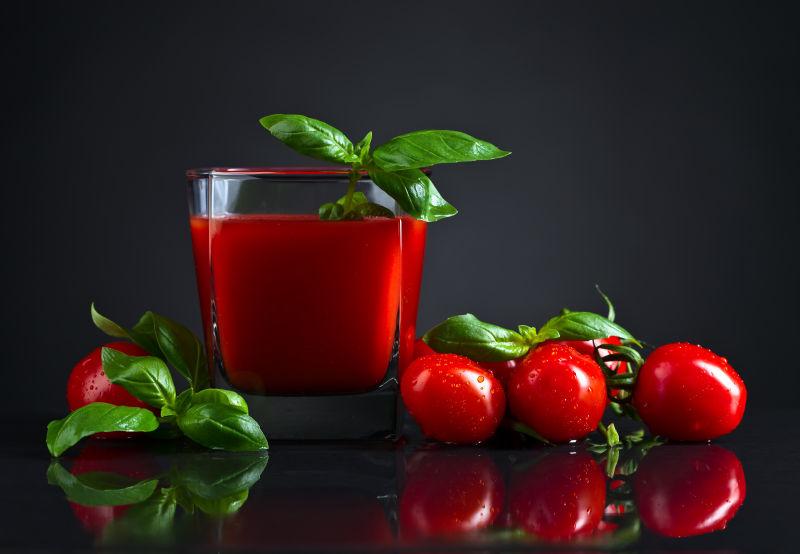 黑色背景下的红色番茄汁和美味的小番茄