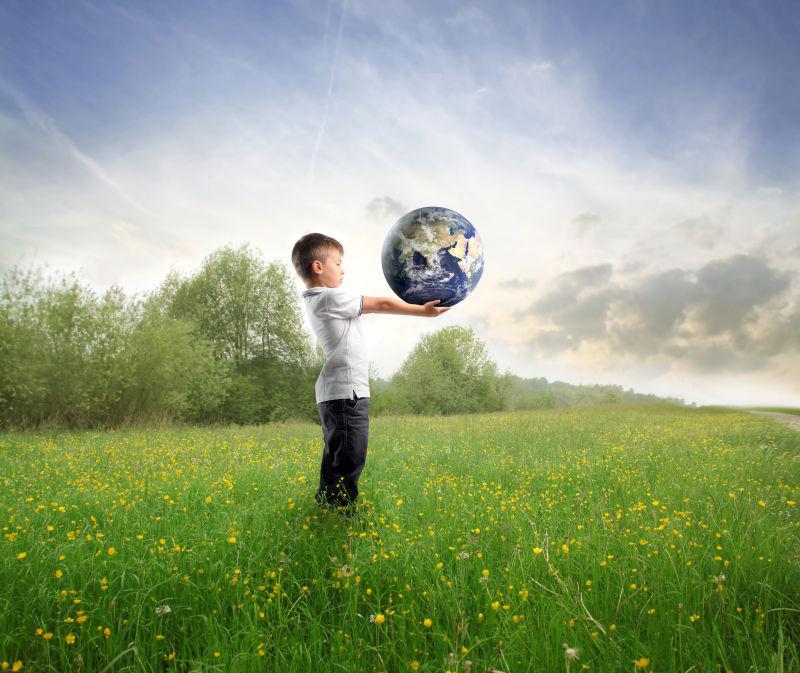 站在草地上的小男孩手中托着的模拟地球