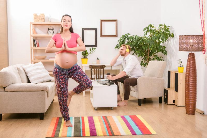 做瑜伽的孕妇和带着耳机玩游戏的丈夫