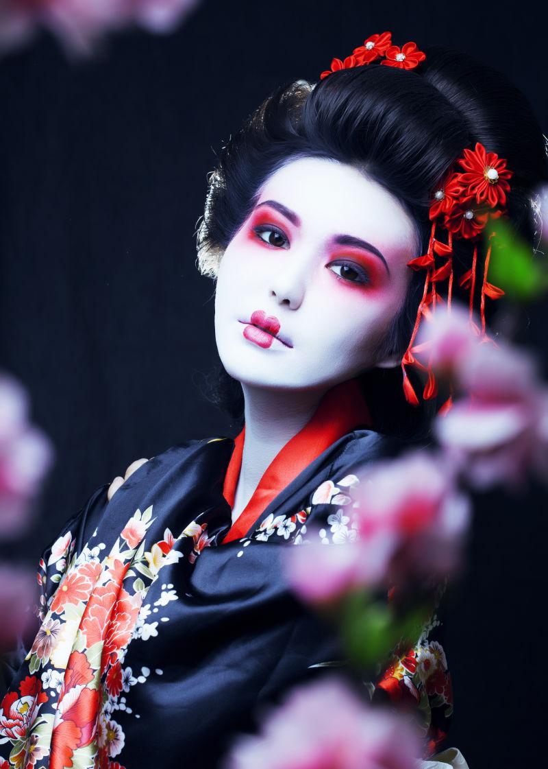和服中的年轻艺妓在黑色背景下投掷樱花