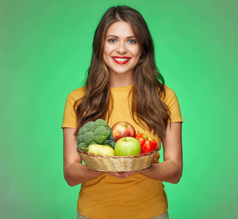 绿色背景前美女拿着装满蔬菜水果的篮子
