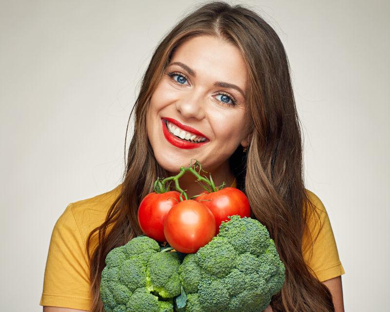 微笑的美女拿着西兰花和番茄