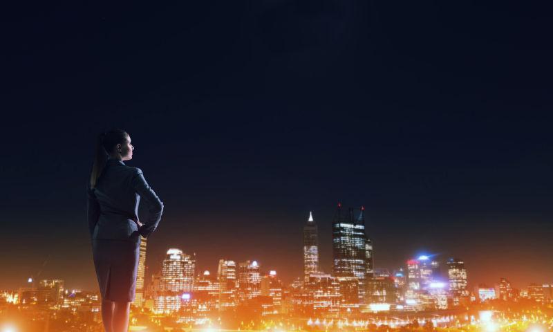穿着黑色职业装的女人看着美丽的城市夜景