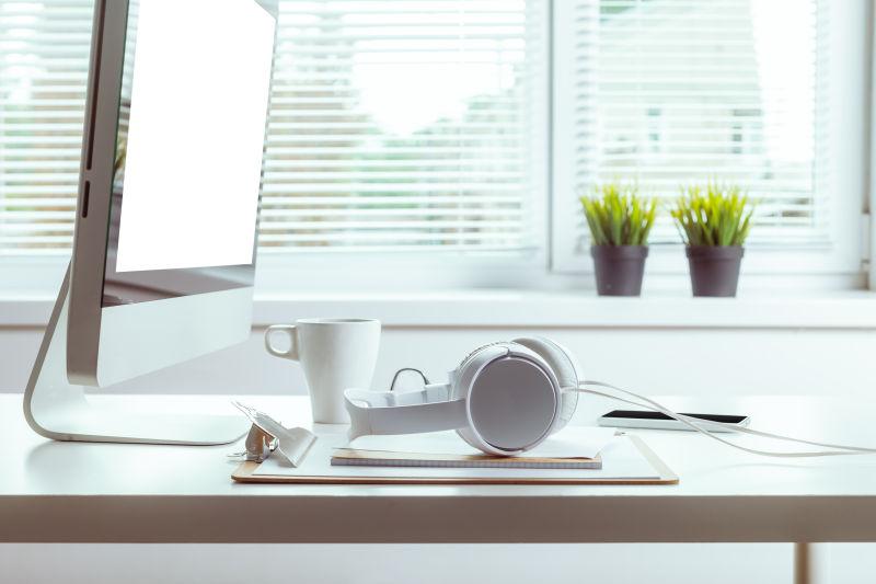 白色办公桌上的苹果电脑和咖啡杯还有白色耳机