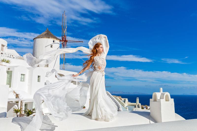 圣托里尼建筑背景下穿白色礼服的美女