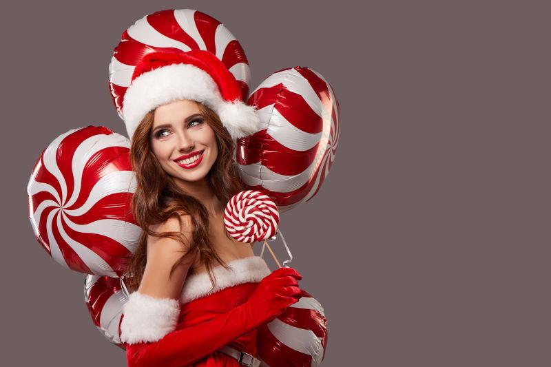 微笑的的圣诞美女拿着棒棒糖和气球