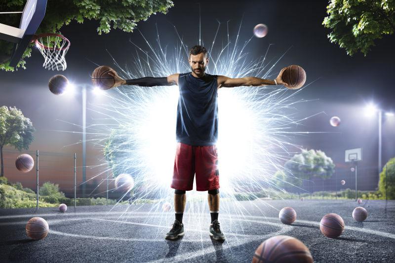 散落着篮球的篮球场上的手里拿着两个篮球背后发着光的运动员