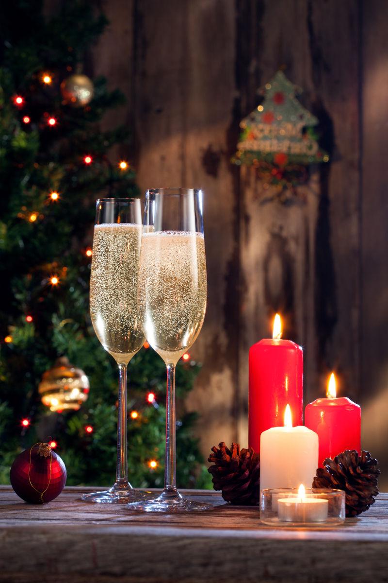 圣诞树边木桌上的两个装着香槟的酒杯和三根点燃的蜡烛